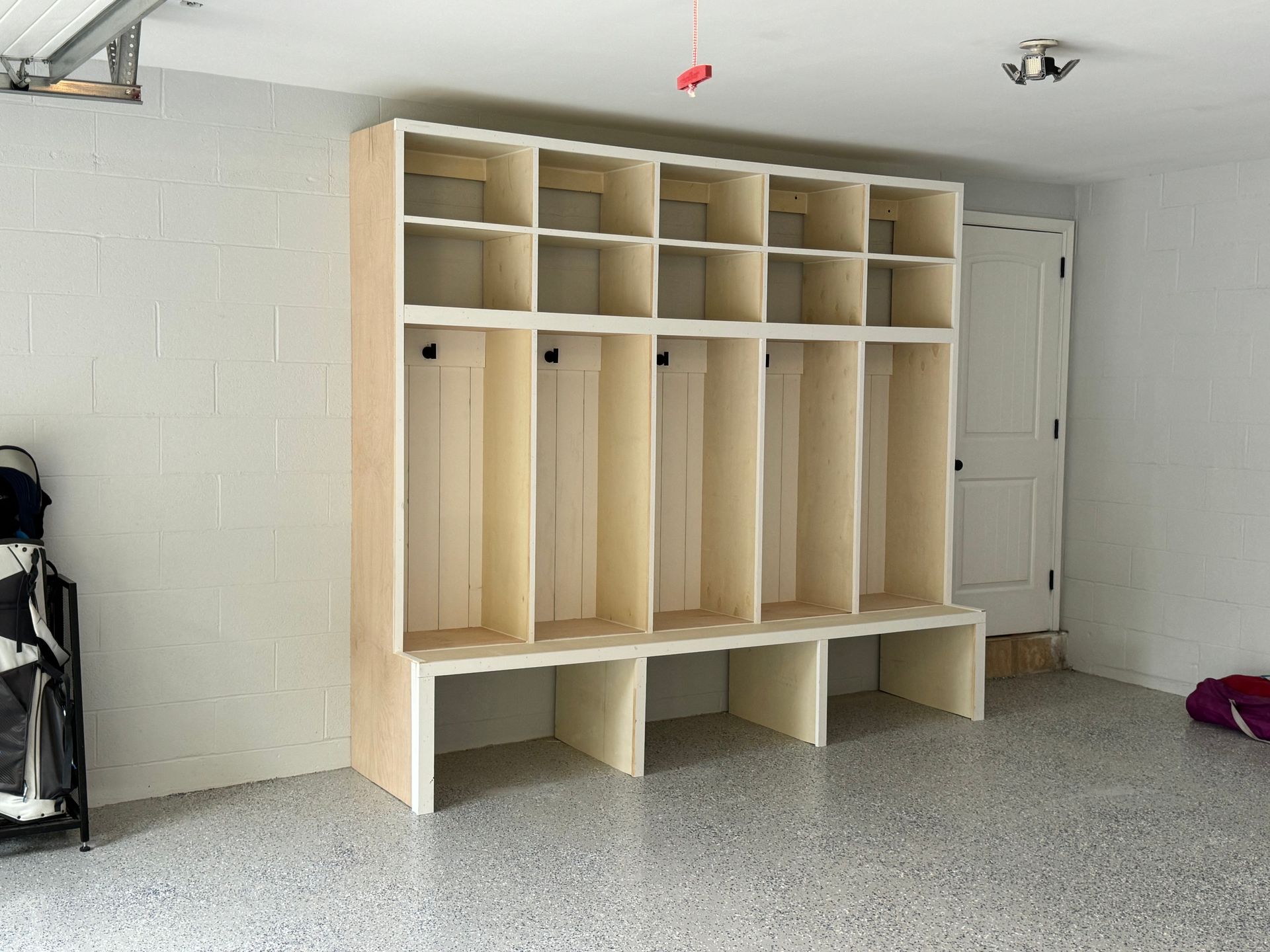 A tall, unfinished wooden locker unit with cubbies, hooks, and a built-in bench, installed against a garage wall.