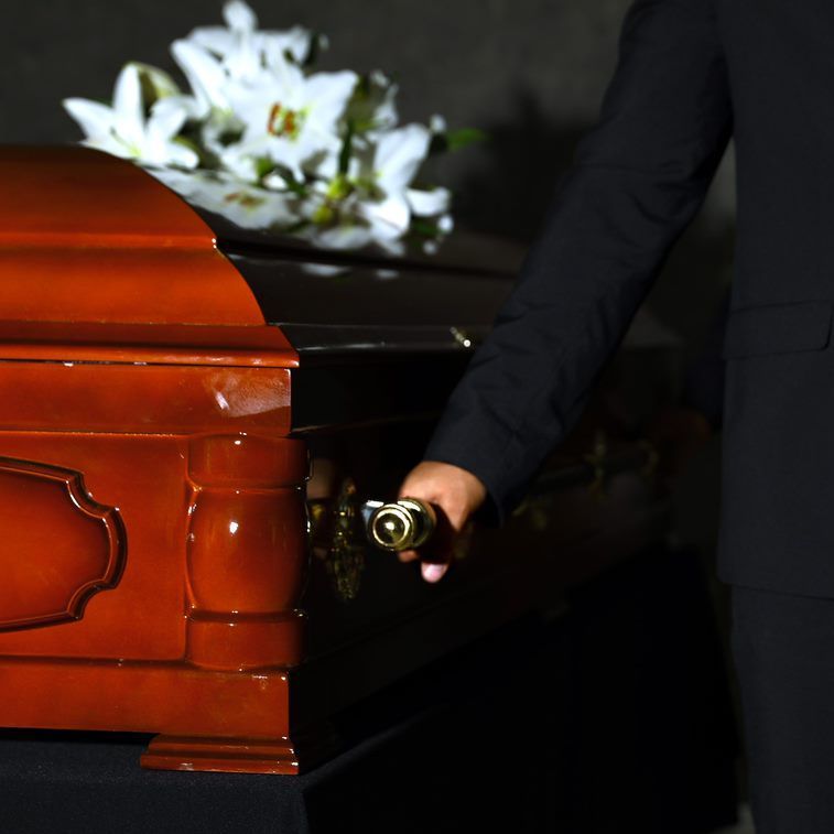 A man in a suit is opening a coffin with flowers in the background.