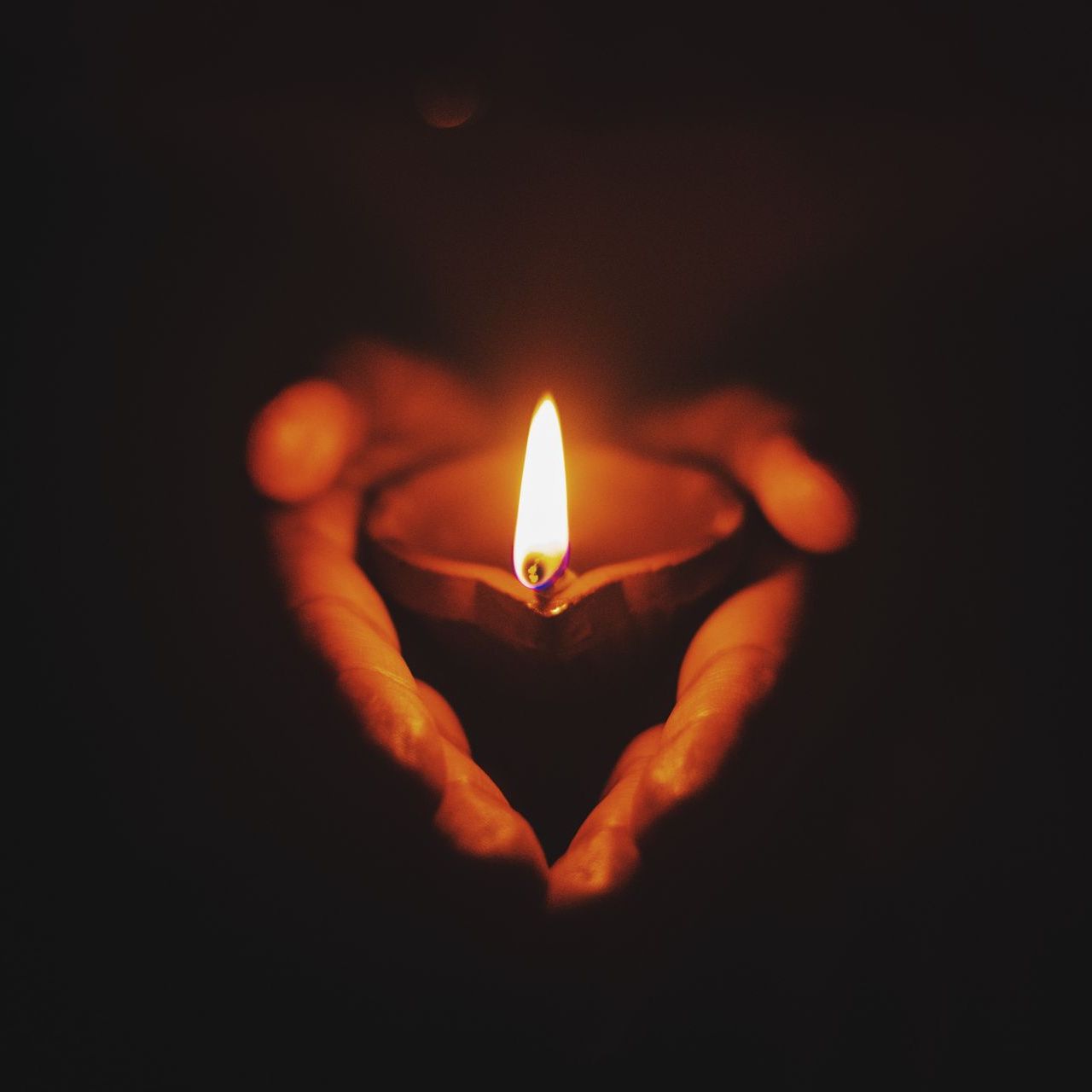 A person is holding a lit candle in their hands in the shape of a heart.