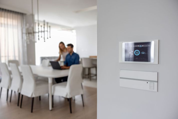 Termostato e interruttore a parete moderni e intelligenti in una luminosa sala da pranzo con due persone sullo sfondo.