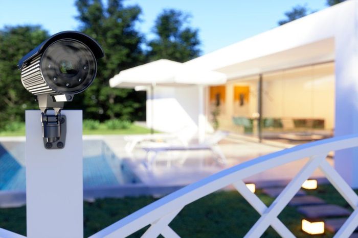 Telecamera di sicurezza su palo bianco accanto a una casa moderna e a una piscina, al crepuscolo.