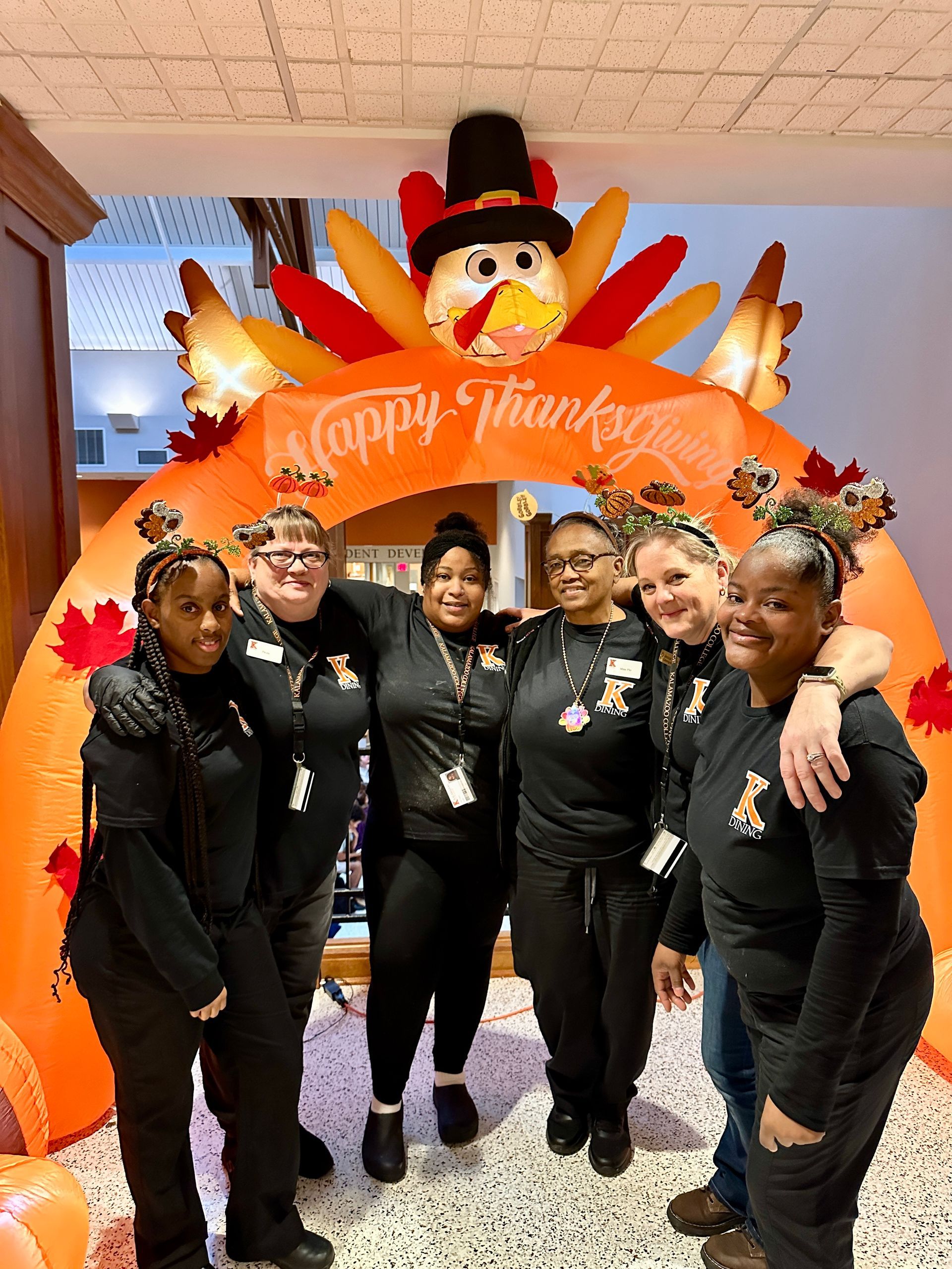 Group of people smiling, posing in a restaurant. Counter in foreground, food service area in background.