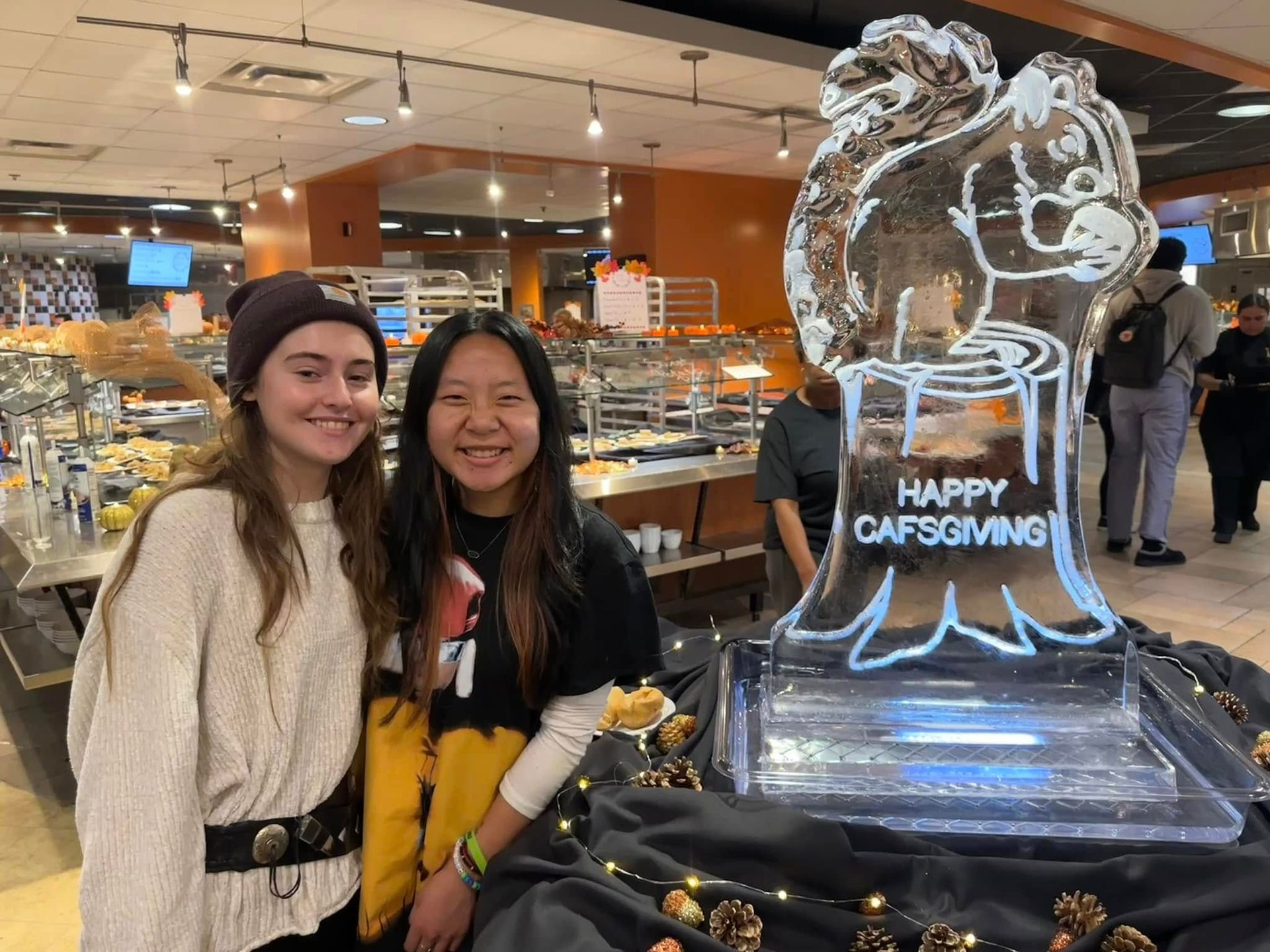Two students posing next to Cafsgiving ice sculpture