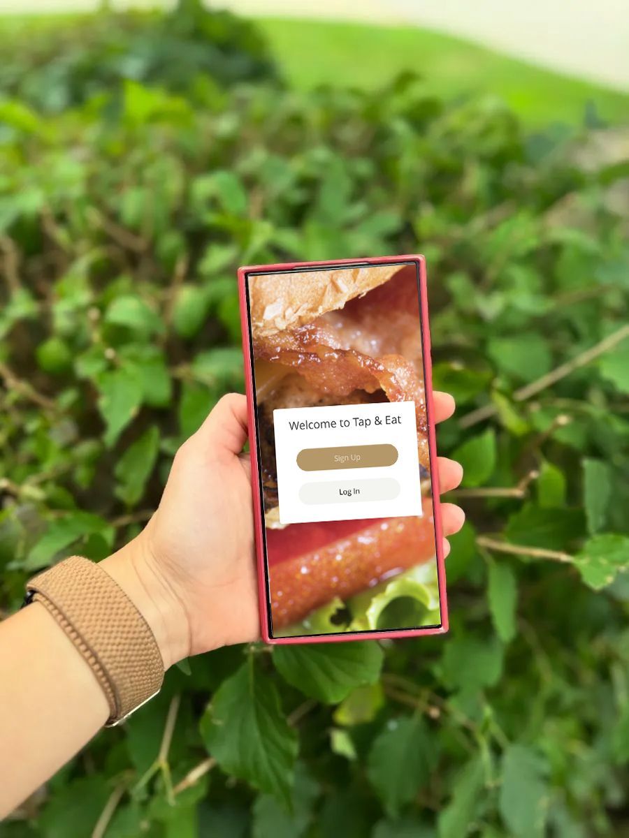 Hand holding a phone displaying a Transact app logo against a backdrop of green foliage.