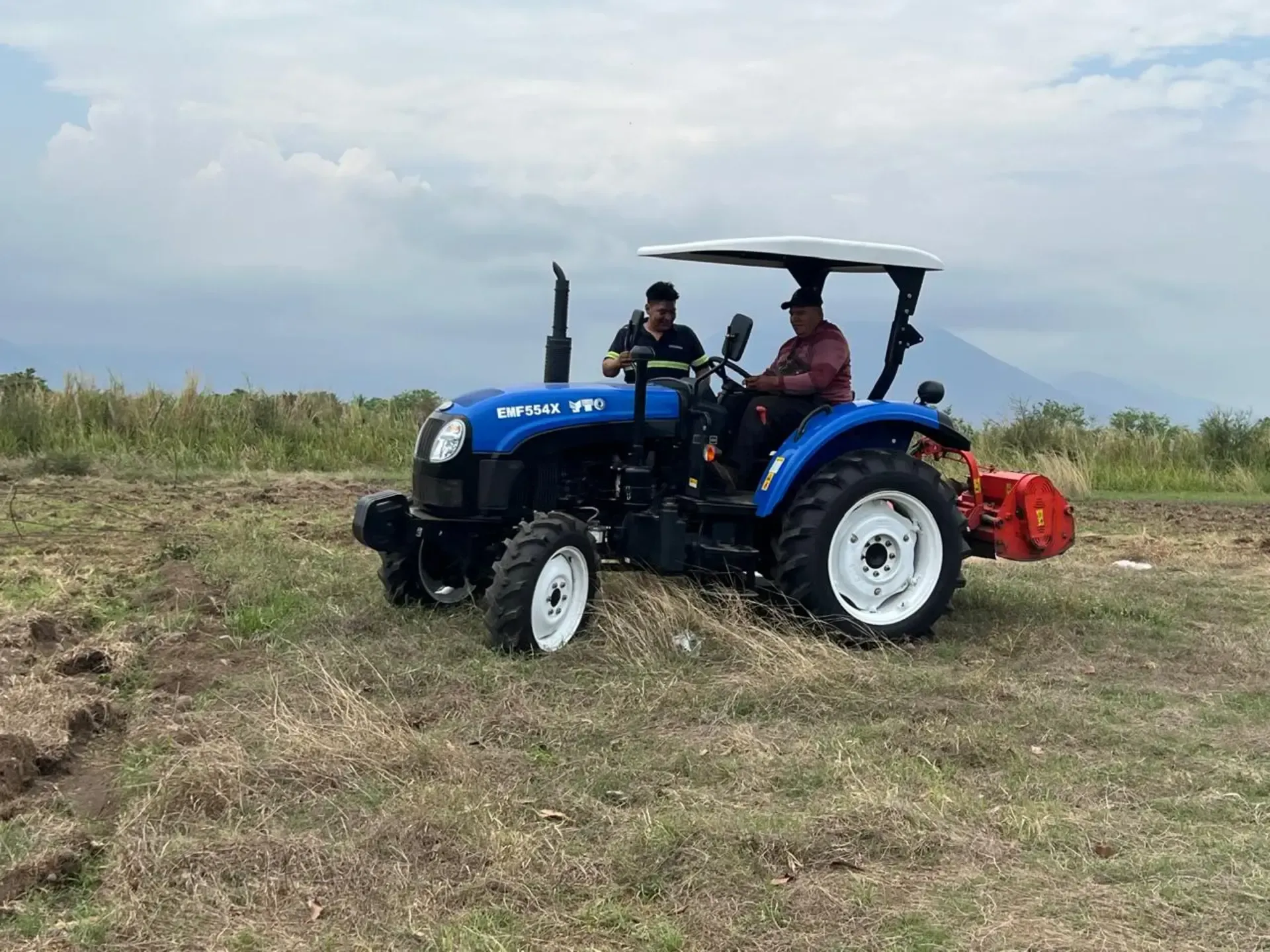 Un hombre conduce un tractor azul en un campo.