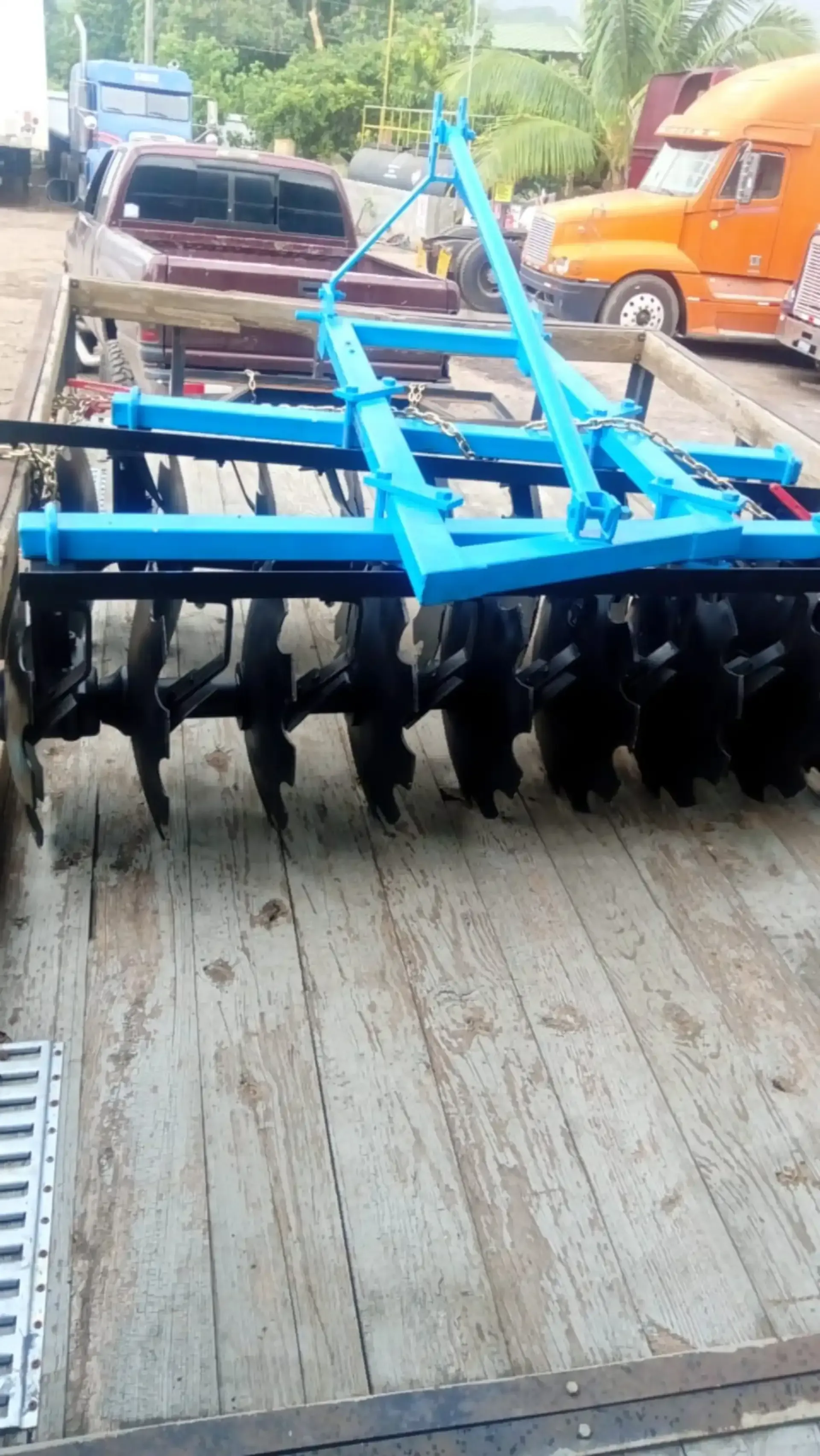 Un arado de disco azul está colocado encima de un remolque de madera.