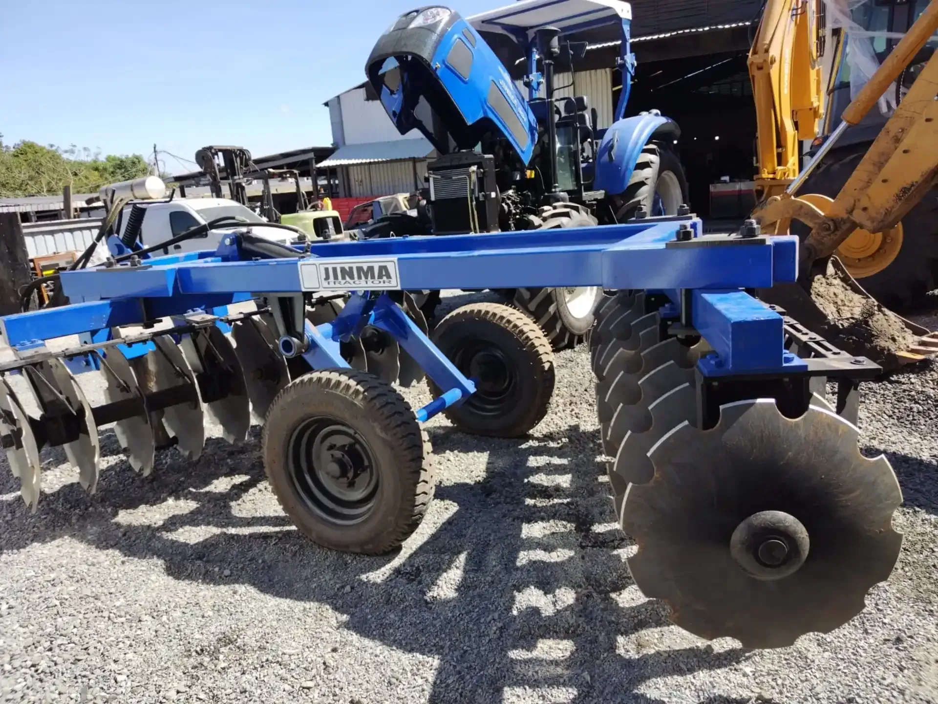 Un tractor azul está estacionado junto a un arado de disco