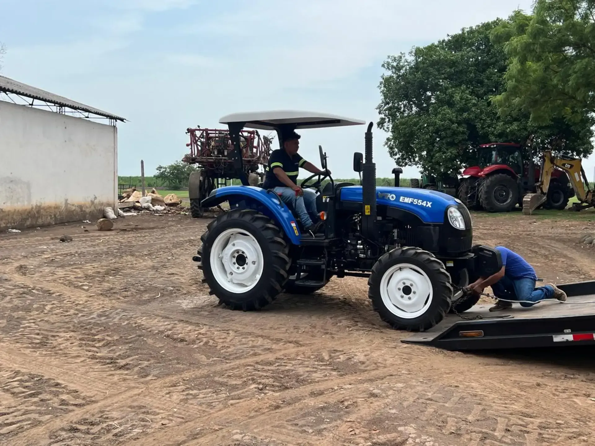 Un hombre conduce un tractor azul en un campo de tierra.
