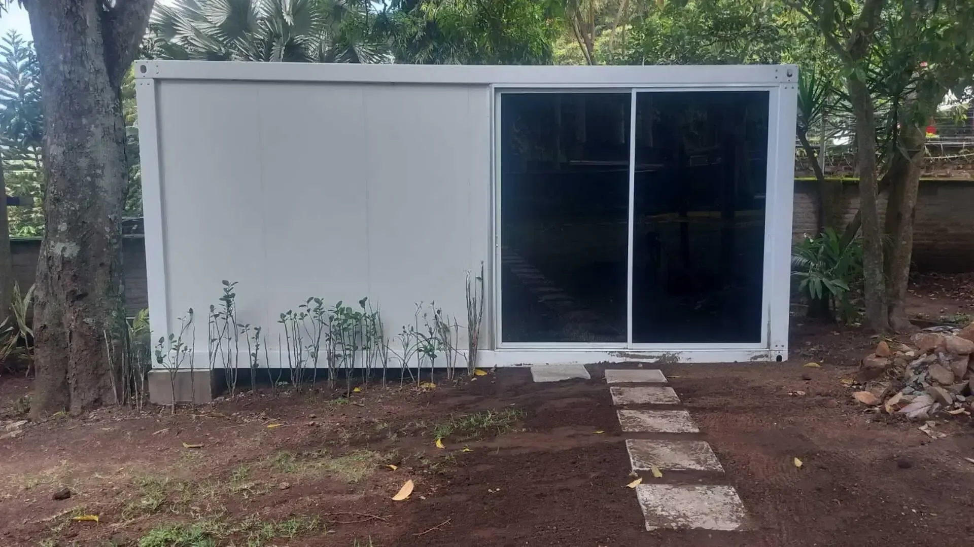Un edificio blanco con una puerta corrediza de vidrio se encuentra en medio de un patio.