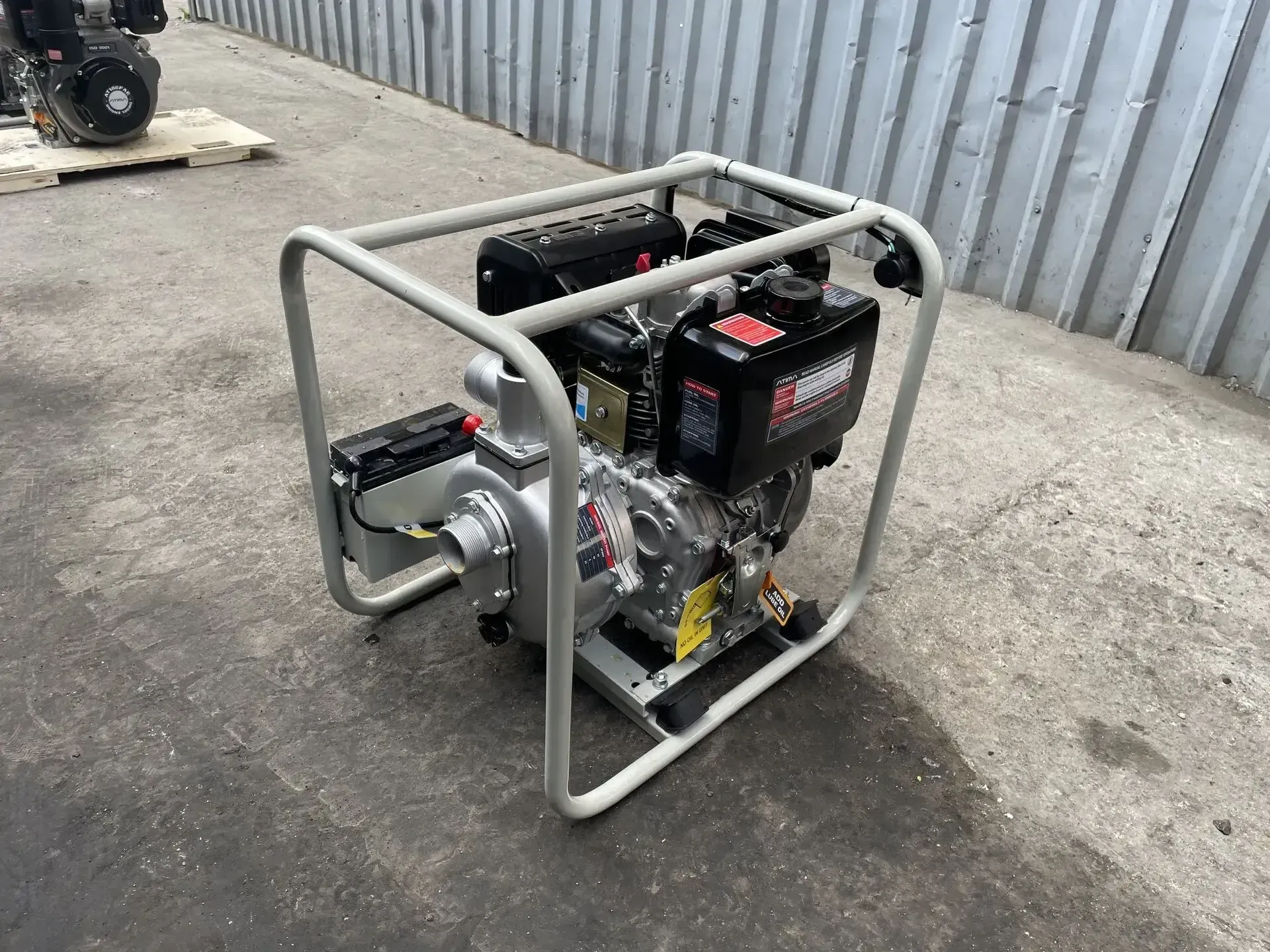 Una bomba de agua alimentada por gas está colocada en el suelo frente a una valla.