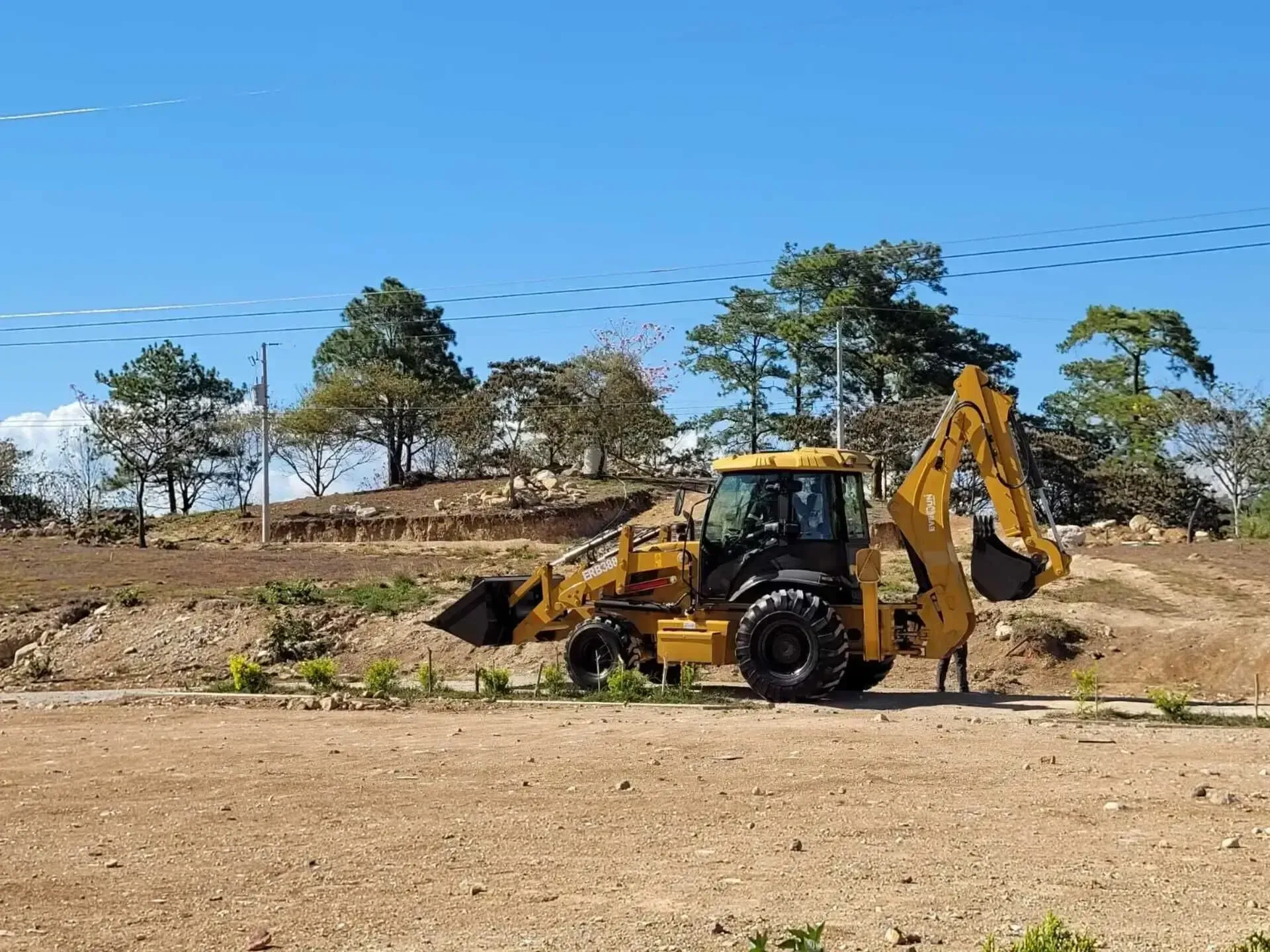 Una retroexcavadora amarilla está estacionada en medio de un campo de tierra.