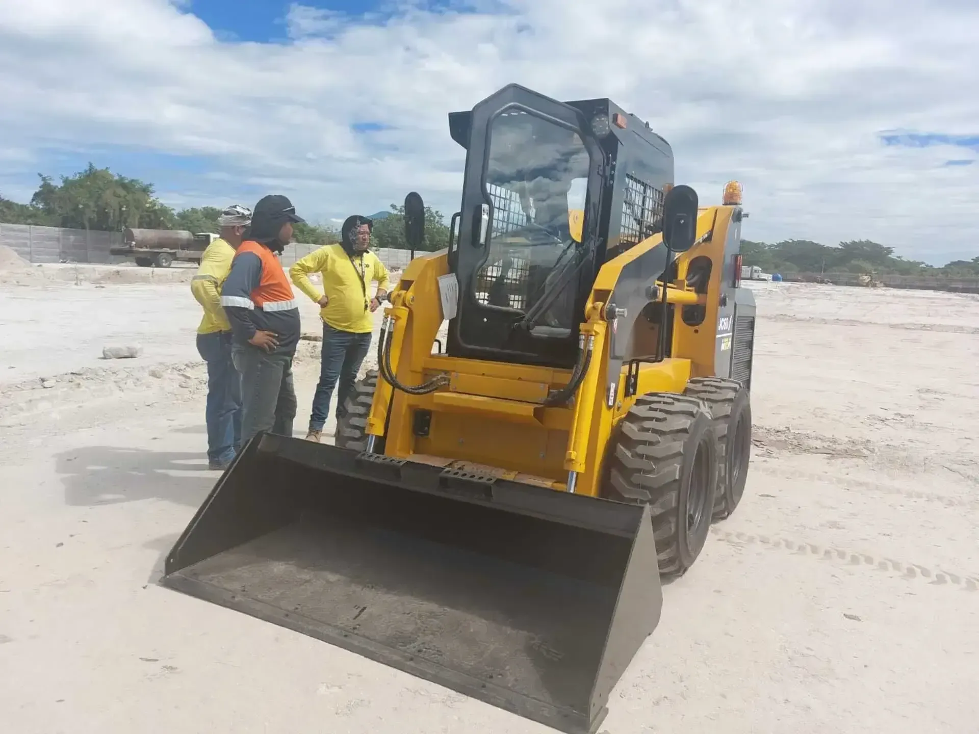 Un grupo de personas está parada alrededor de una topadora amarilla en un campo de tierra.
