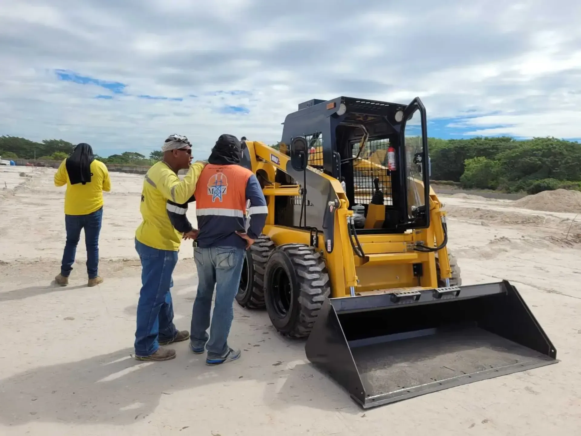 Un grupo de trabajadores de la construcción está parado frente a una topadora amarilla.