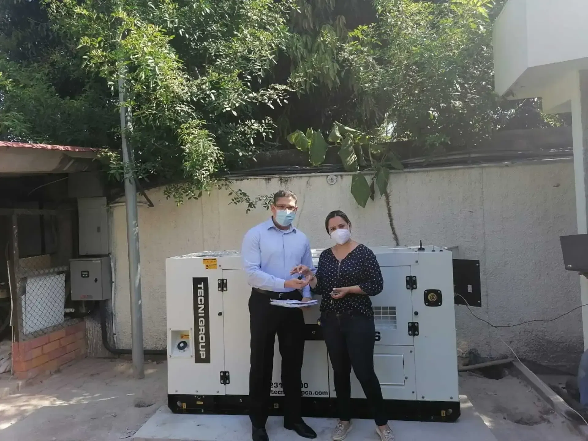 Un hombre y una mujer con máscaras se paran frente a un generador