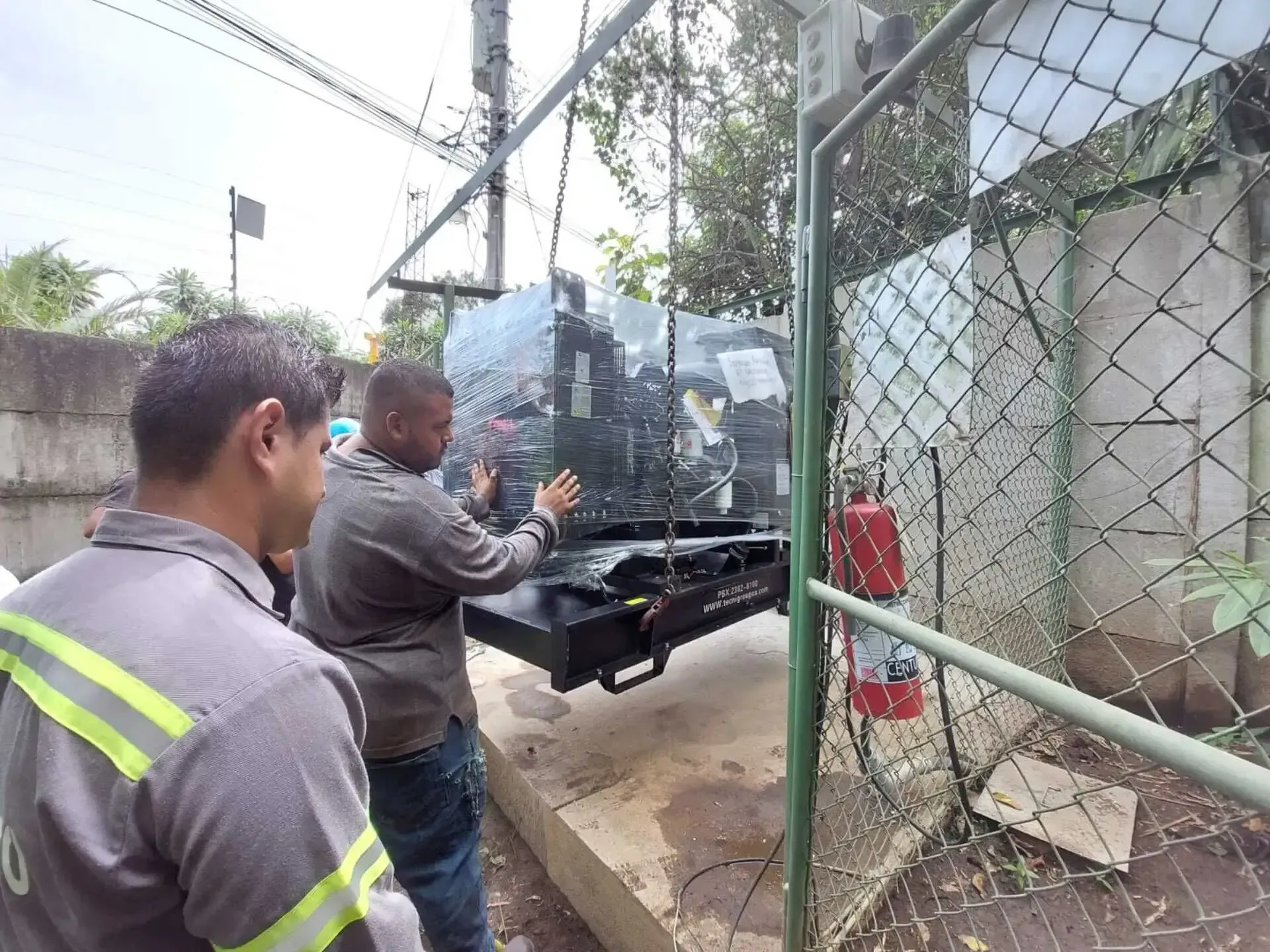 Dos hombres están trabajando en una máquina detrás de una valla metálica.