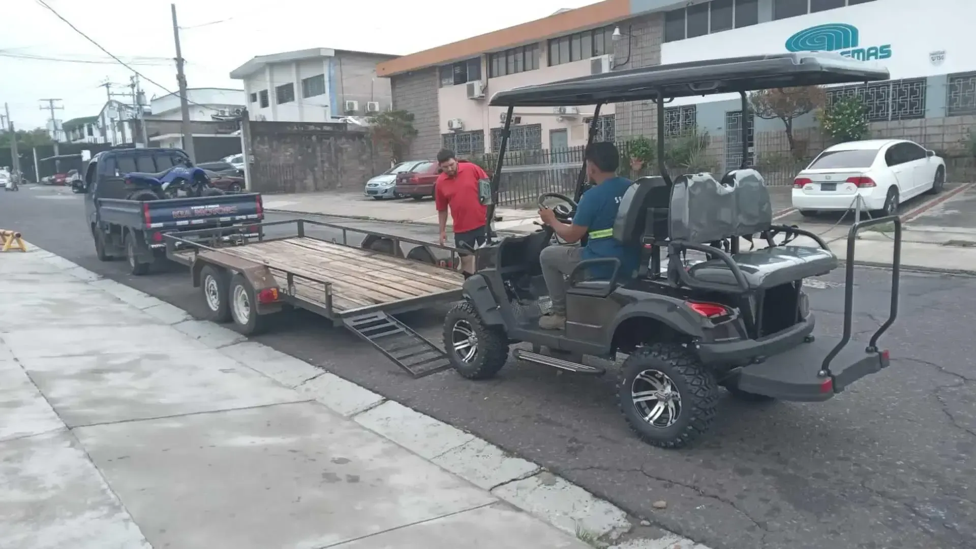 Un camión sobre un remolque remolca un carrito de golf.