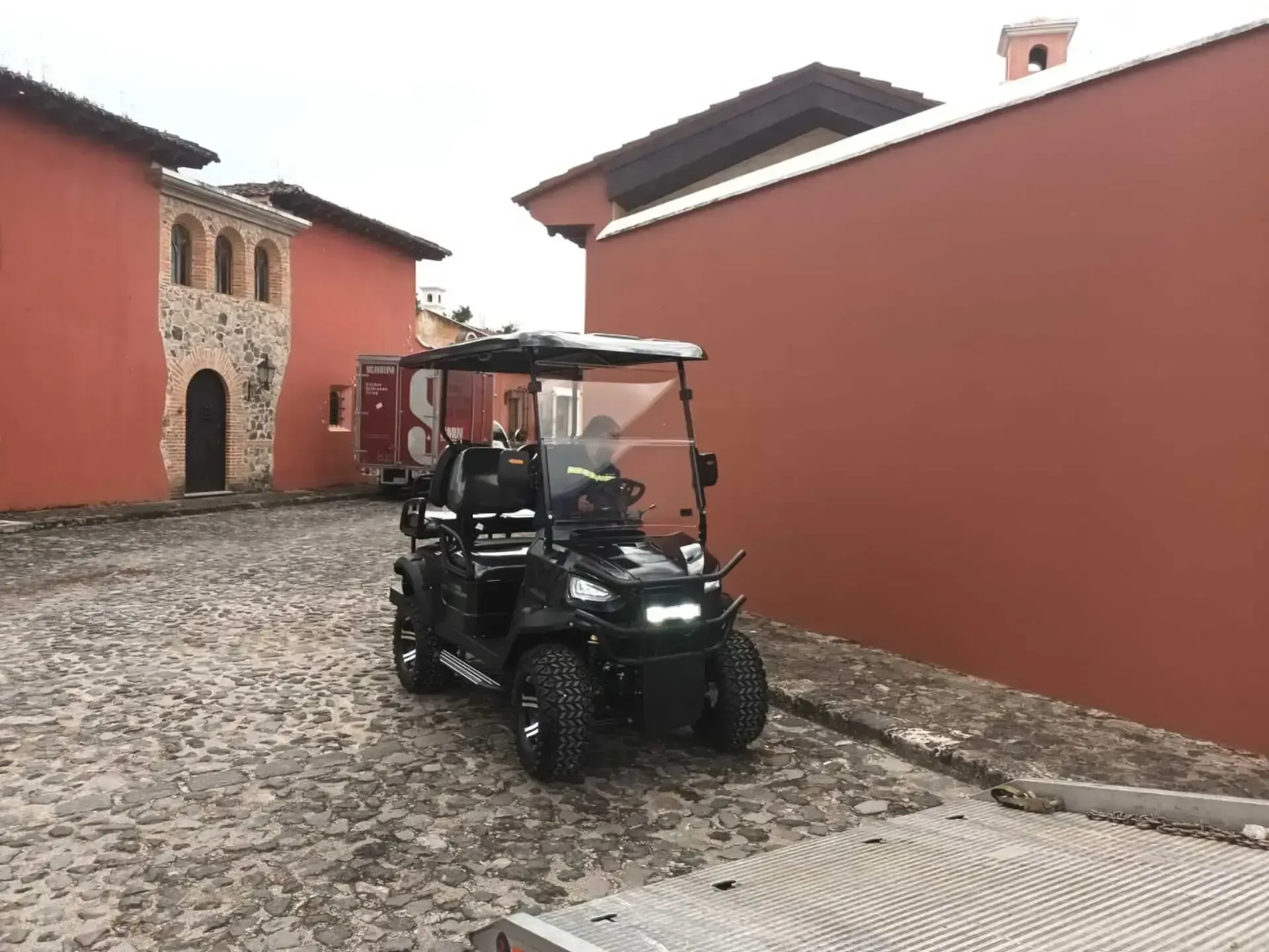 Un carrito de golf está estacionado en una calle adoquinada frente a un edificio rojo.