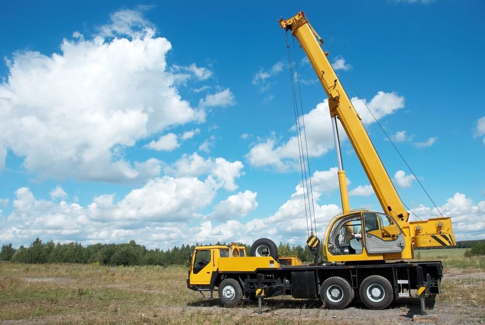 Yellow mobile crane on a truck chassis against a blue sky with clouds in a field.