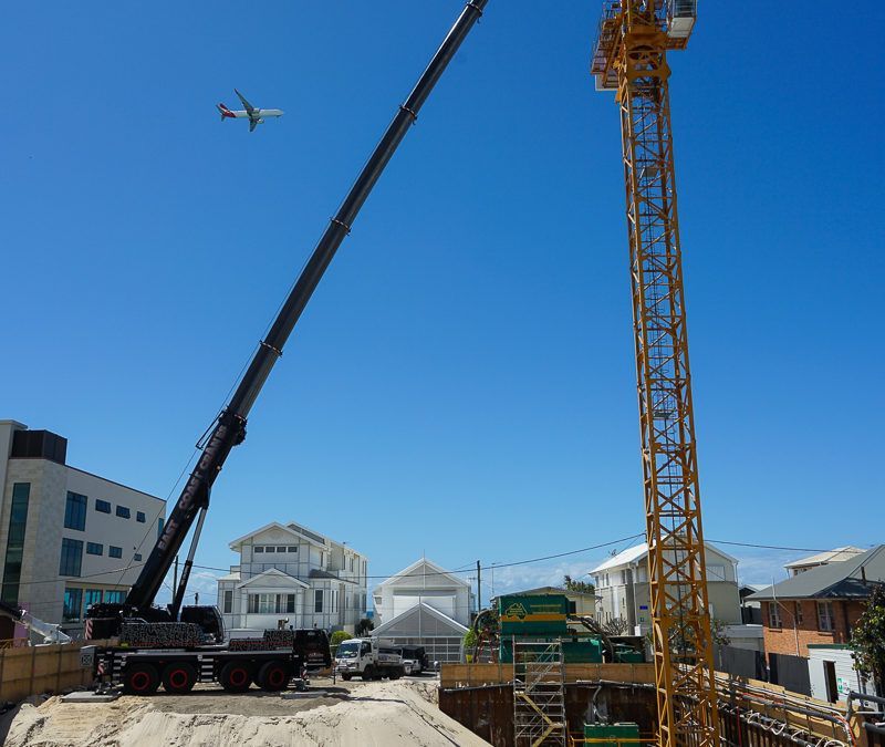 A Plane Is Flying Over a Construction Site with A Crane in The Foreground — East Coast Cranes in Ormeau, QLD