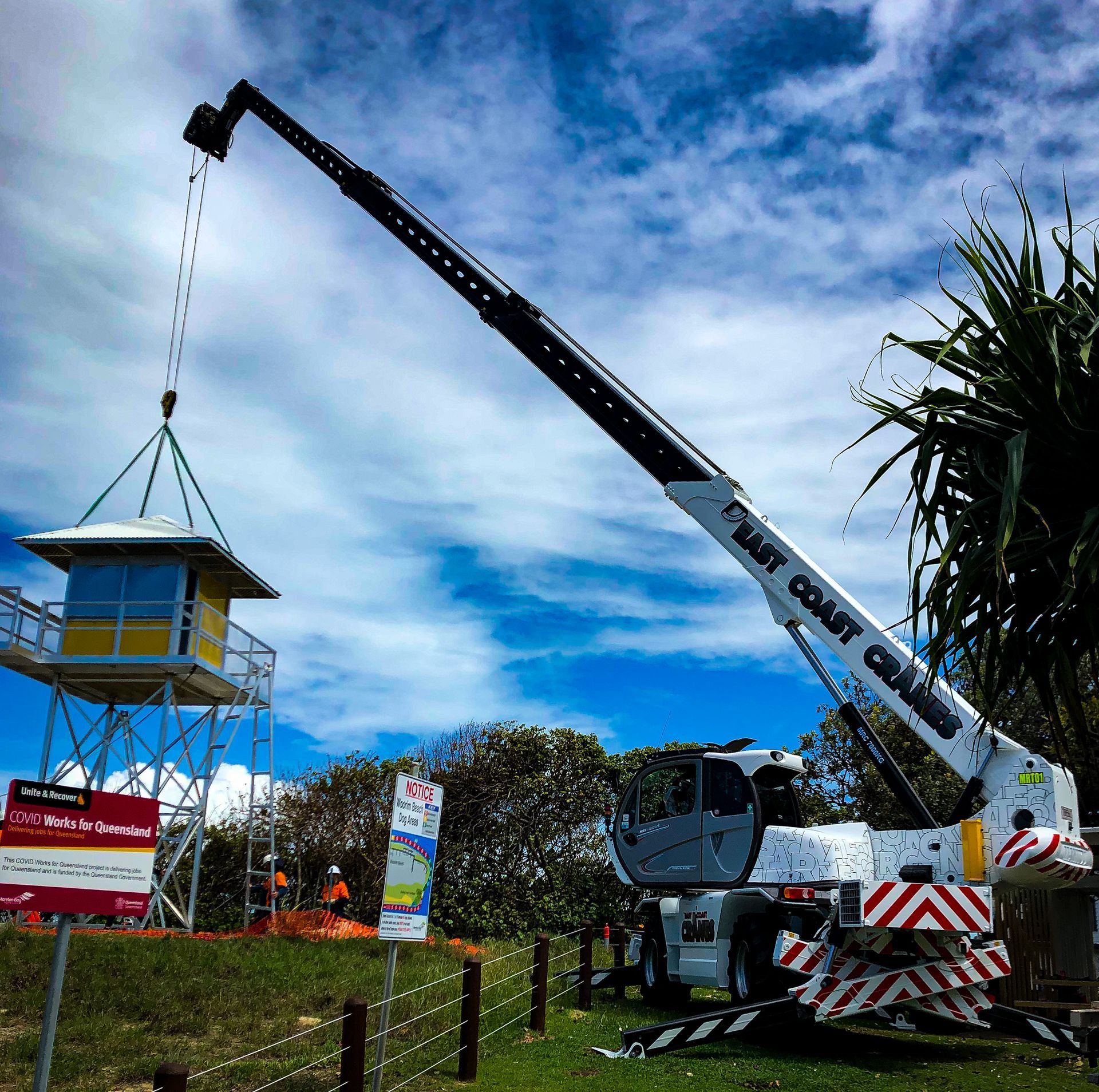 Crane Lifting a Yellow Lifeguard Tower Into Place Near a Beach. Sunny Day With Blue Sky and Some Greener