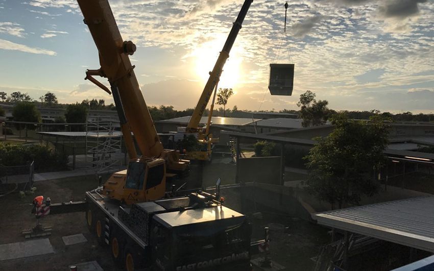 A Large Yellow Crane Is Lifting a Large Box in The Air — East Coast Cranes in Ormeau, QLD