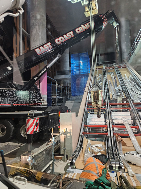 A Crane Lifting Materials in an Interior Construction Site. Worker in Orange Vest Nearby — East Coast Cranes in Ormeau, QLD
