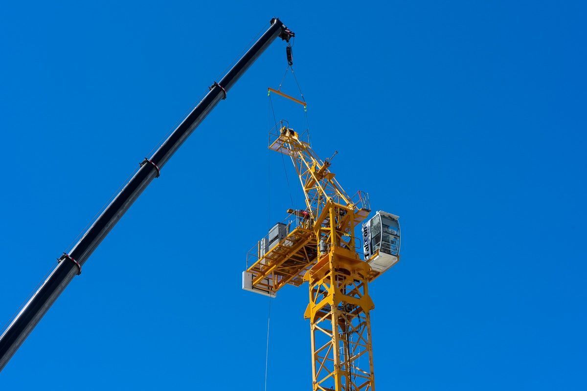 A Construction Crane Is Being Lifted by A Crane Against a Blue Sky — East Coast Cranes in Ormeau, QLD