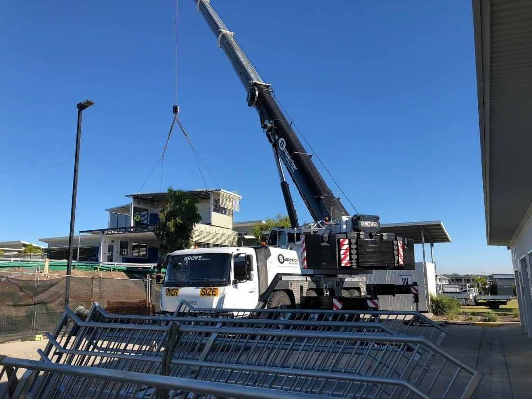 A Large Crane Is Lifting a Fence in Front of A Building — East Coast Cranes in Ormeau, QLD