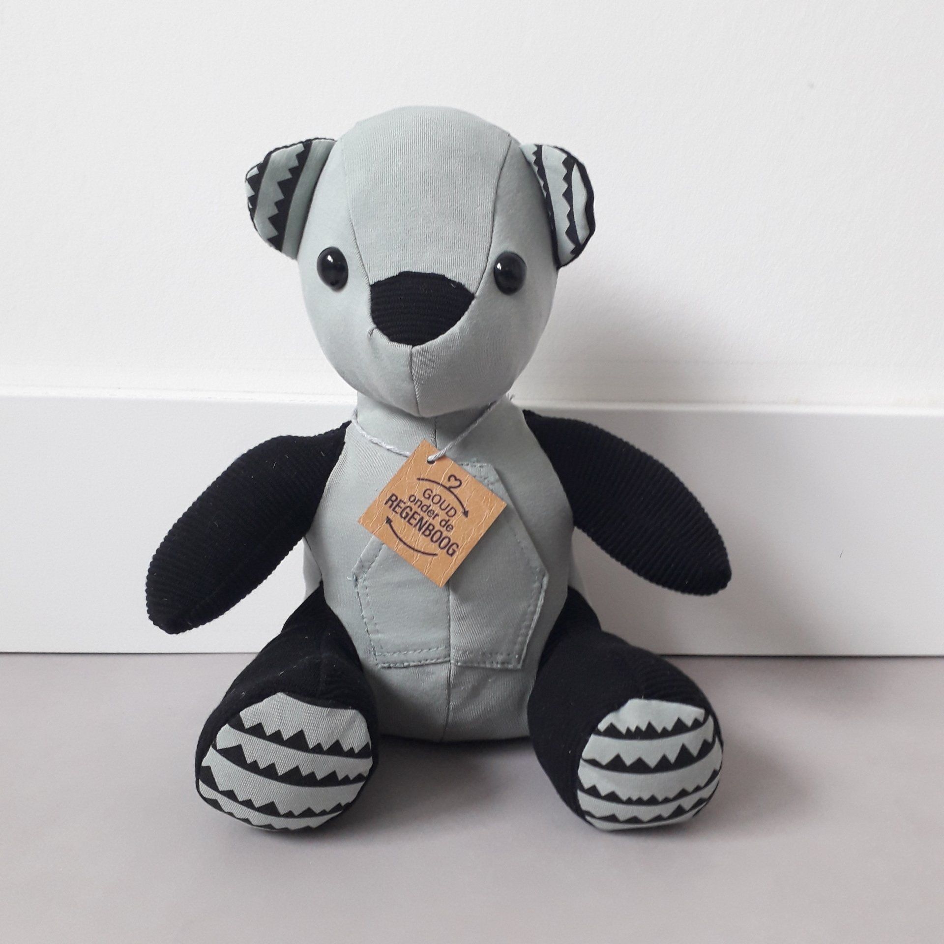 Een grijze en zwarte herinneringsbeer met een label eraan gemaakt van eerste babykleding