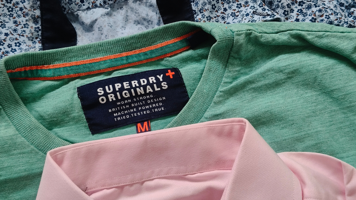 A green Superdry Originals t-shirt with a size M label, layered beneath a light pink polo shirt.