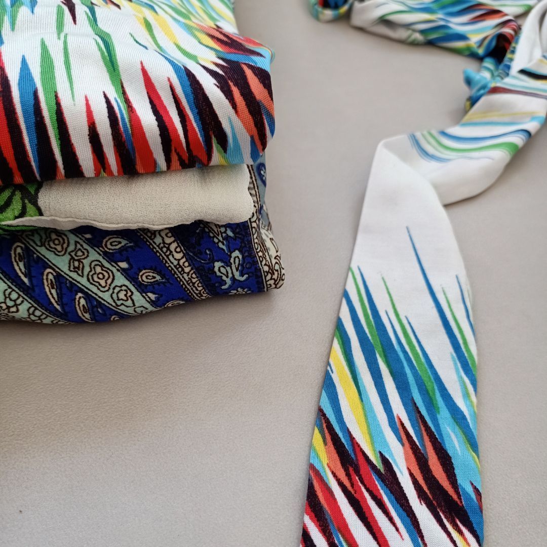 Een stropdas met een kleurrijk patroon ligt naast een stapel kleding