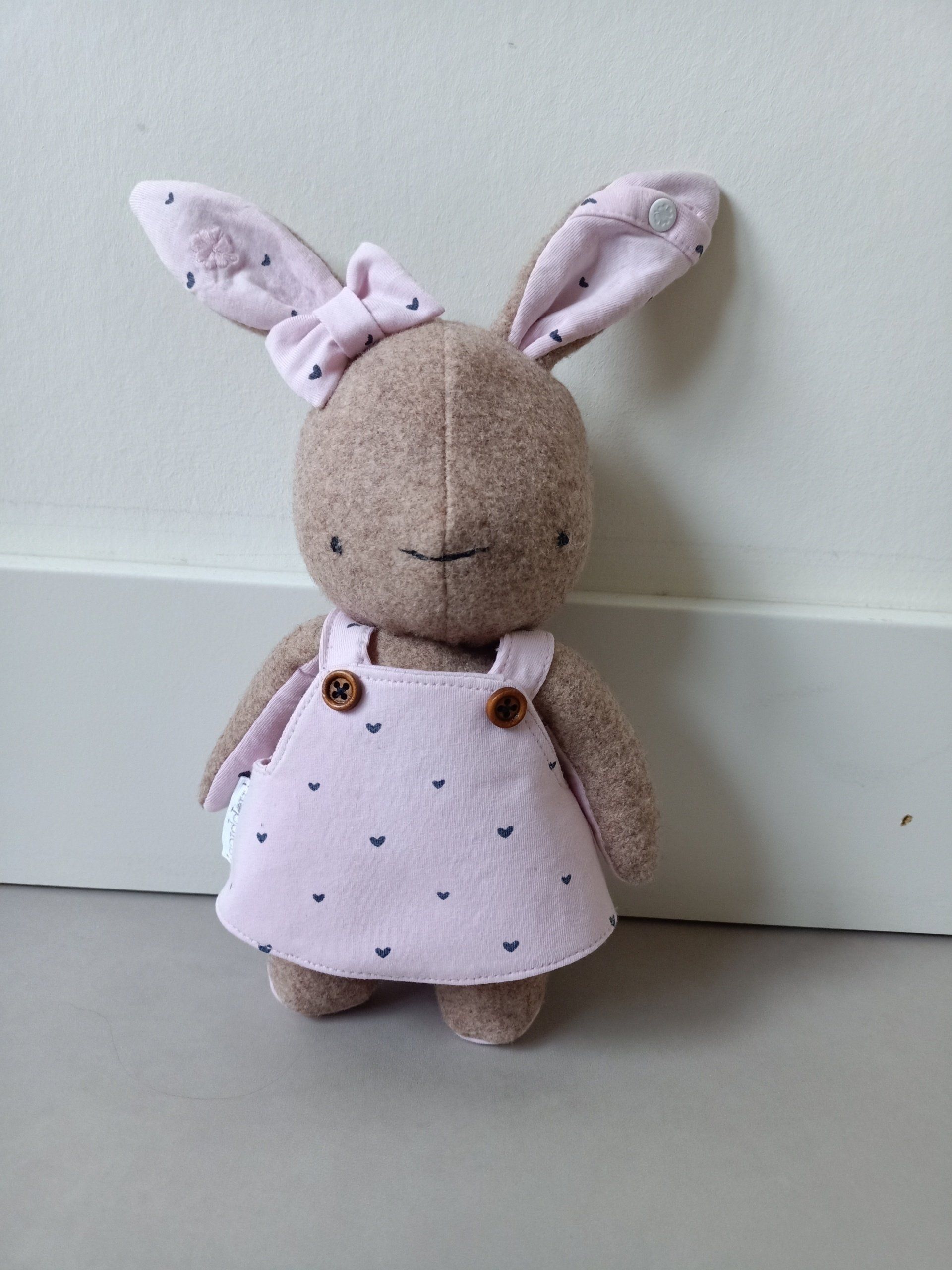 Een herinneringshaasje met een roze jurk staat naast een muur.