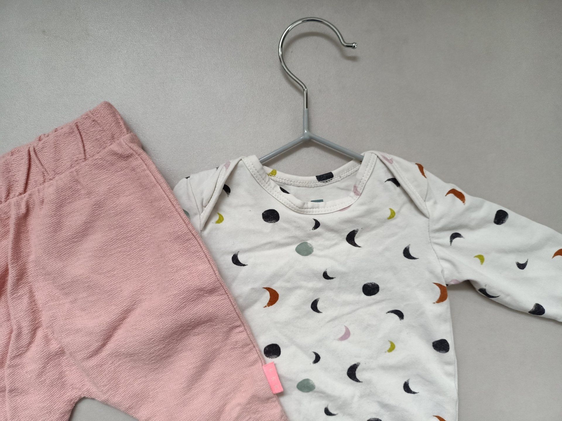 De kleertjes van een baby hangen aan een kleerhanger op een tafel.