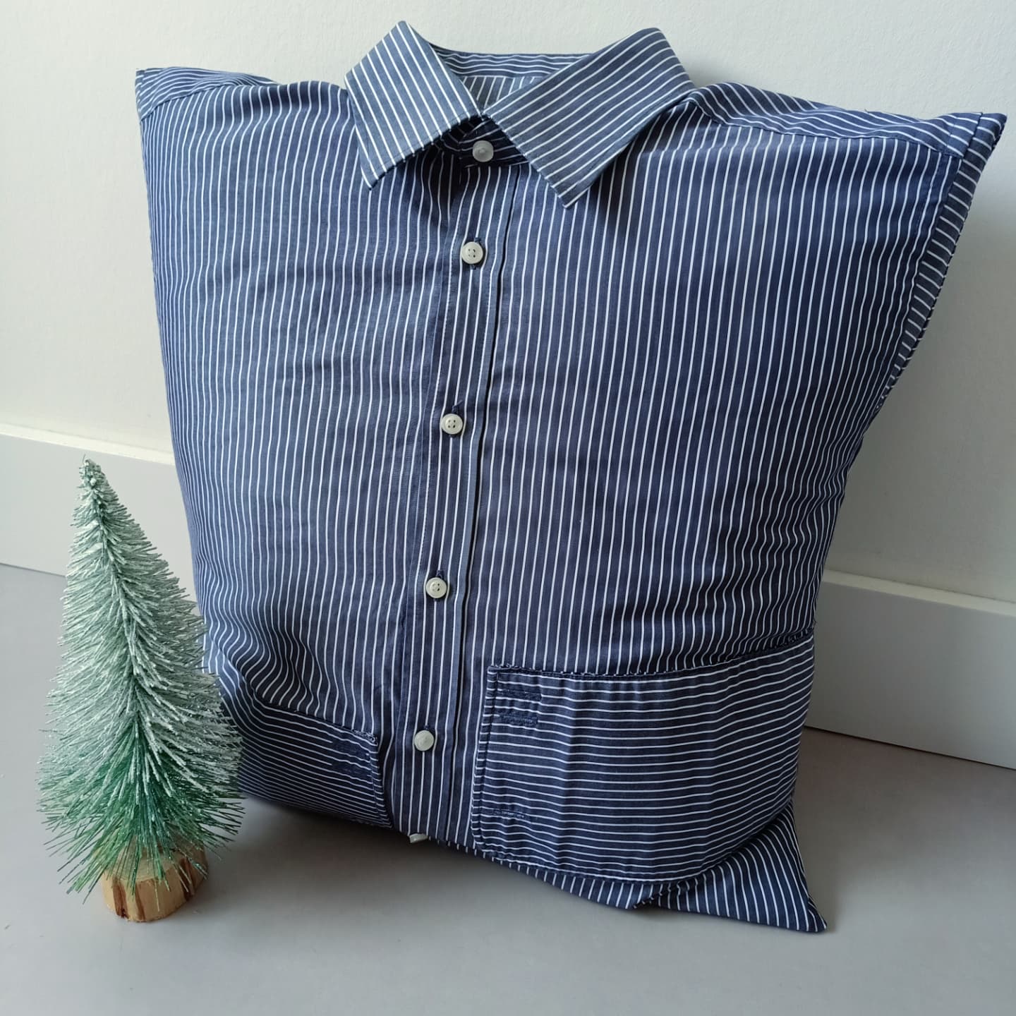 Een blauw-wit gestreept overhemdkussen ligt naast een kleine kerstboom.
