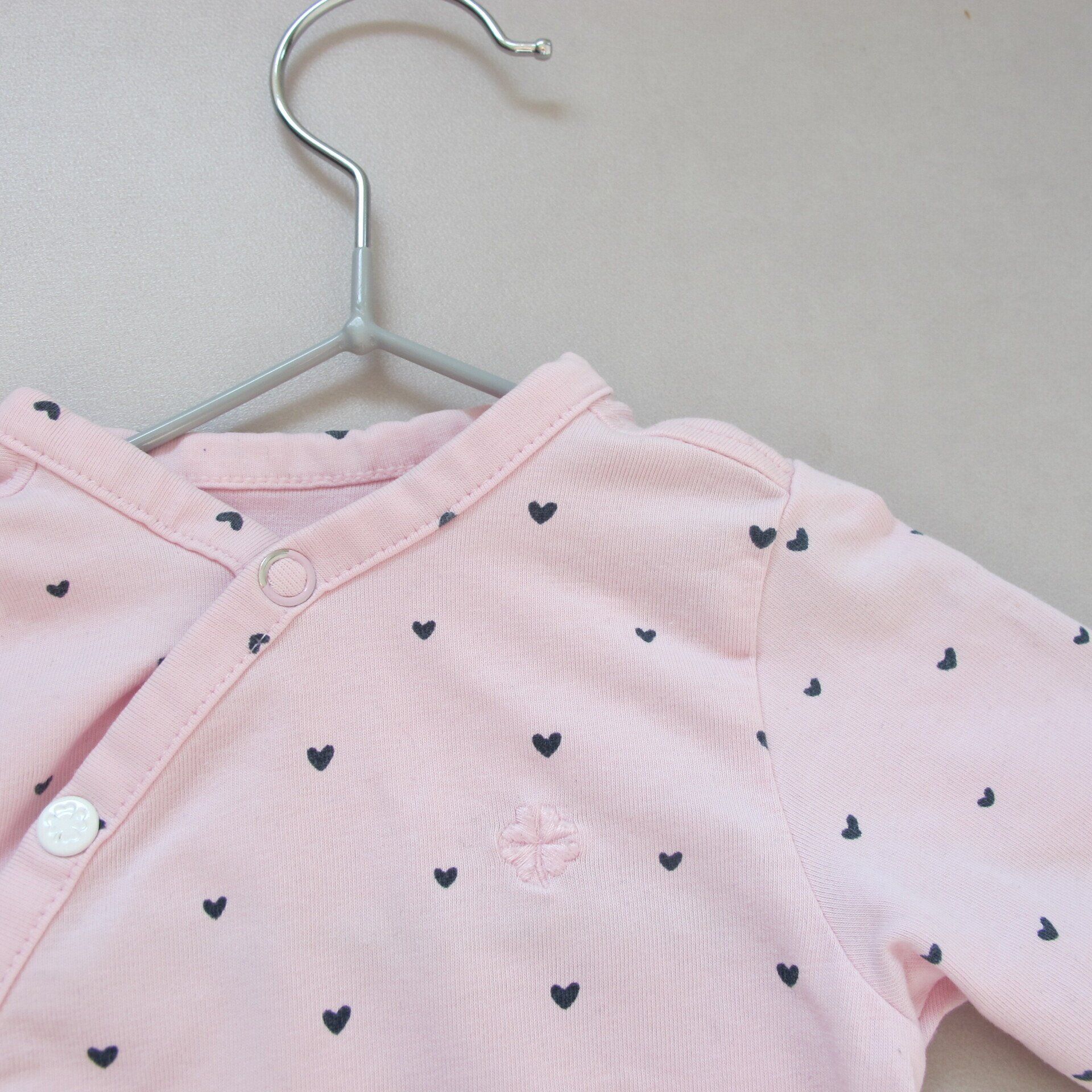 Een roze shirt met zwarte hartjes erop hangt aan een hanger