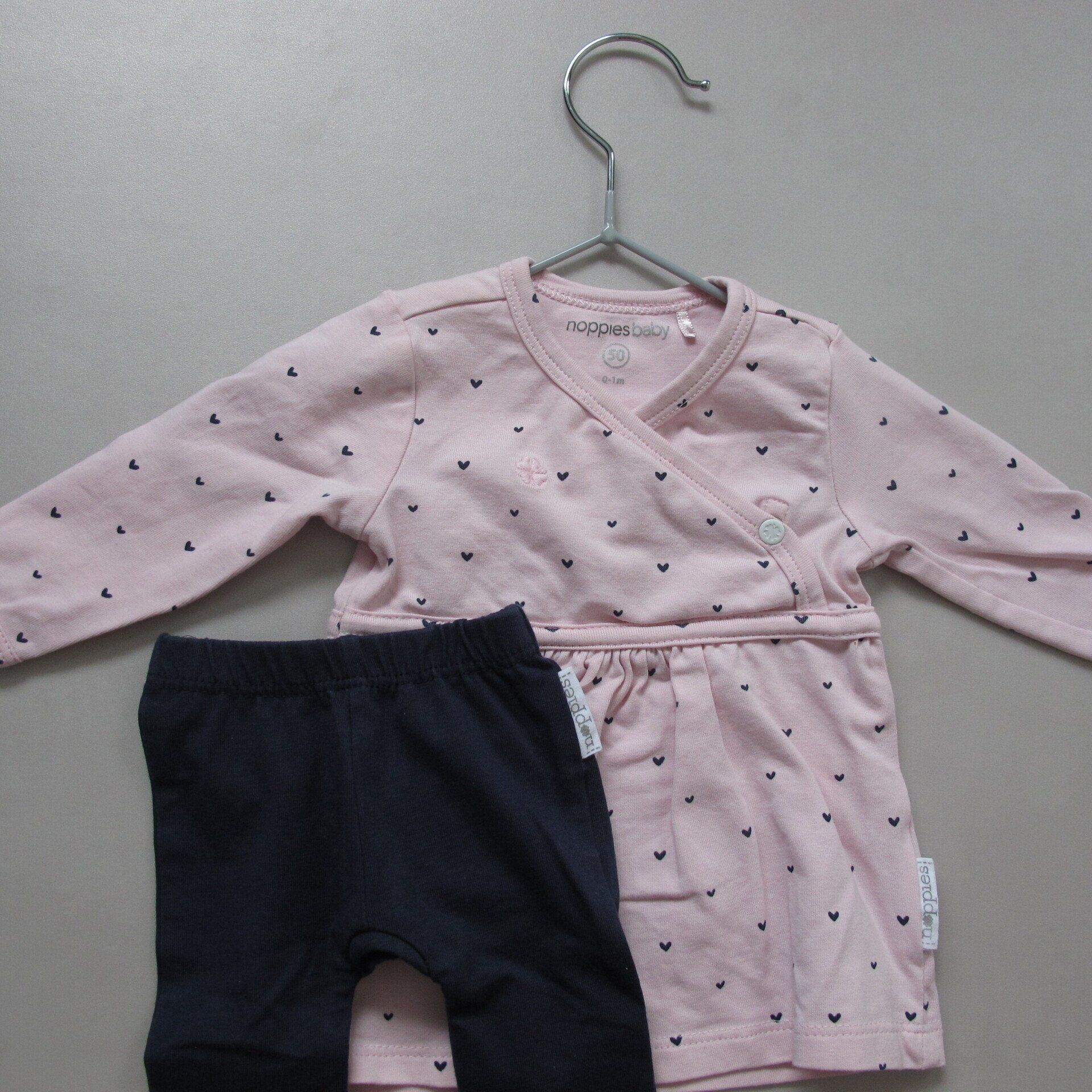 Een roze shirt en een zwarte broek hangen aan een hanger