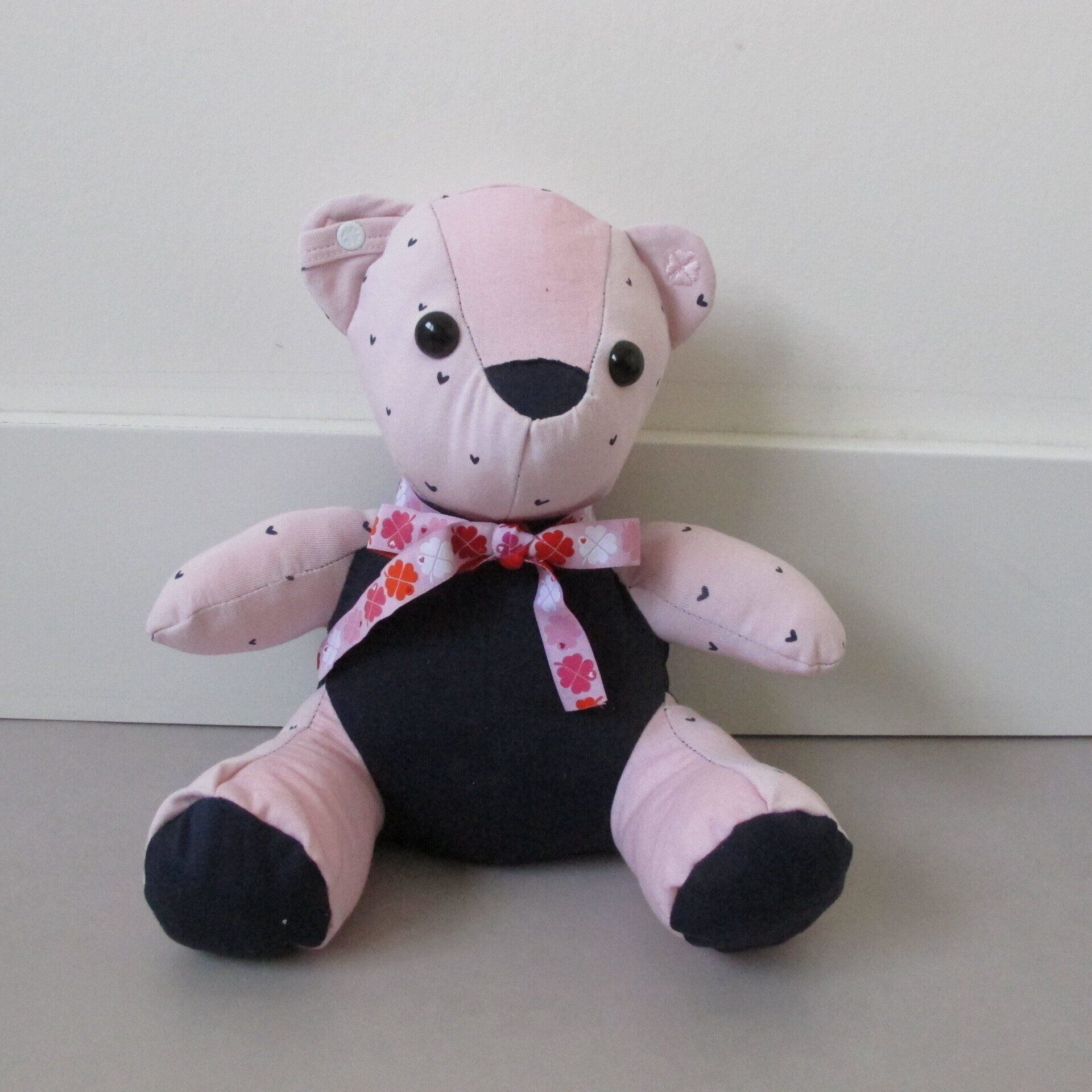 Een roze en zwarte herinneringsbeer met een bloemensjaal om zijn nek gemaakt van eerste babykleding