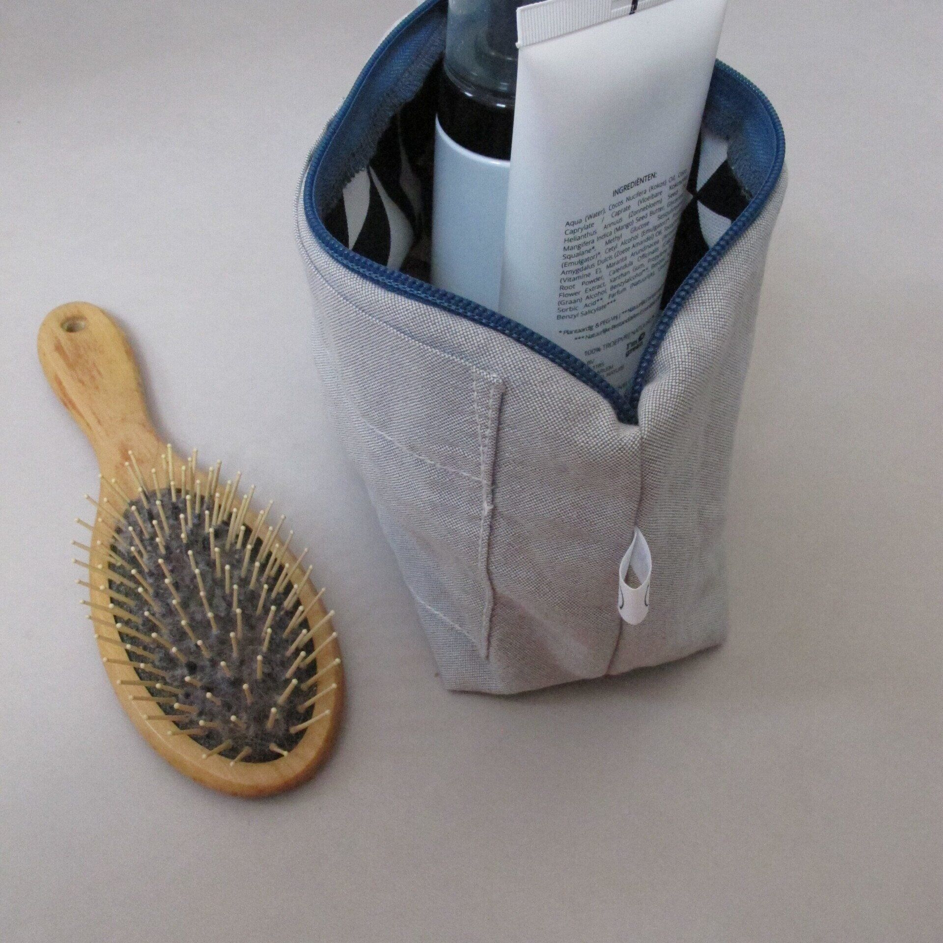 Een borstel ligt naast een cosmetische tas gevuld met lotion en een spuitfles