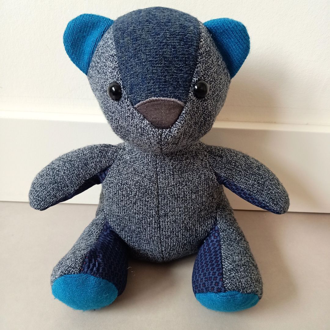 Een blauwe en grijze troostbeer zit op een tafel