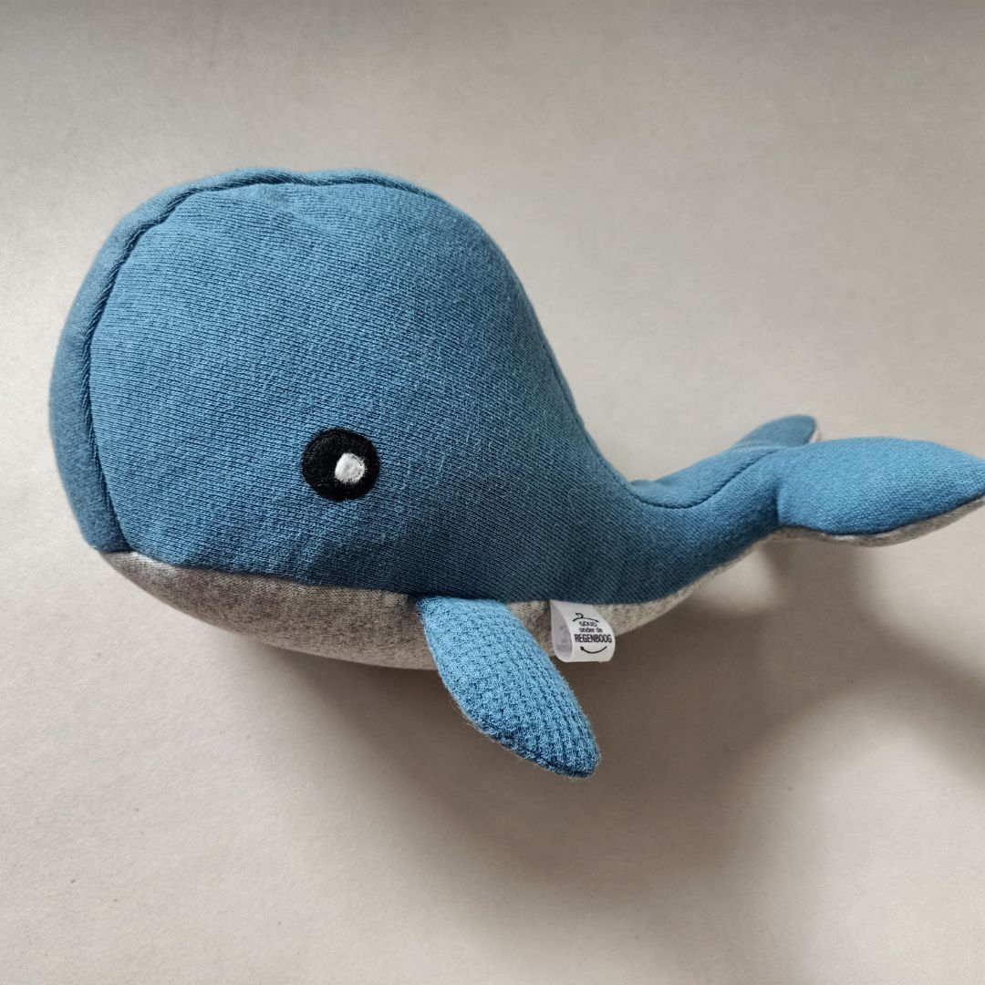 Een herinneringsknuffel in de vorm van een walvis op een wit oppervlak.