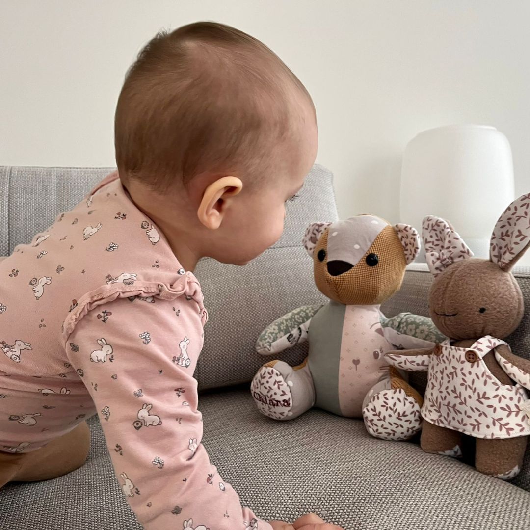 Een baby kruipt op een bank naar twee herinneringsknuffels.
