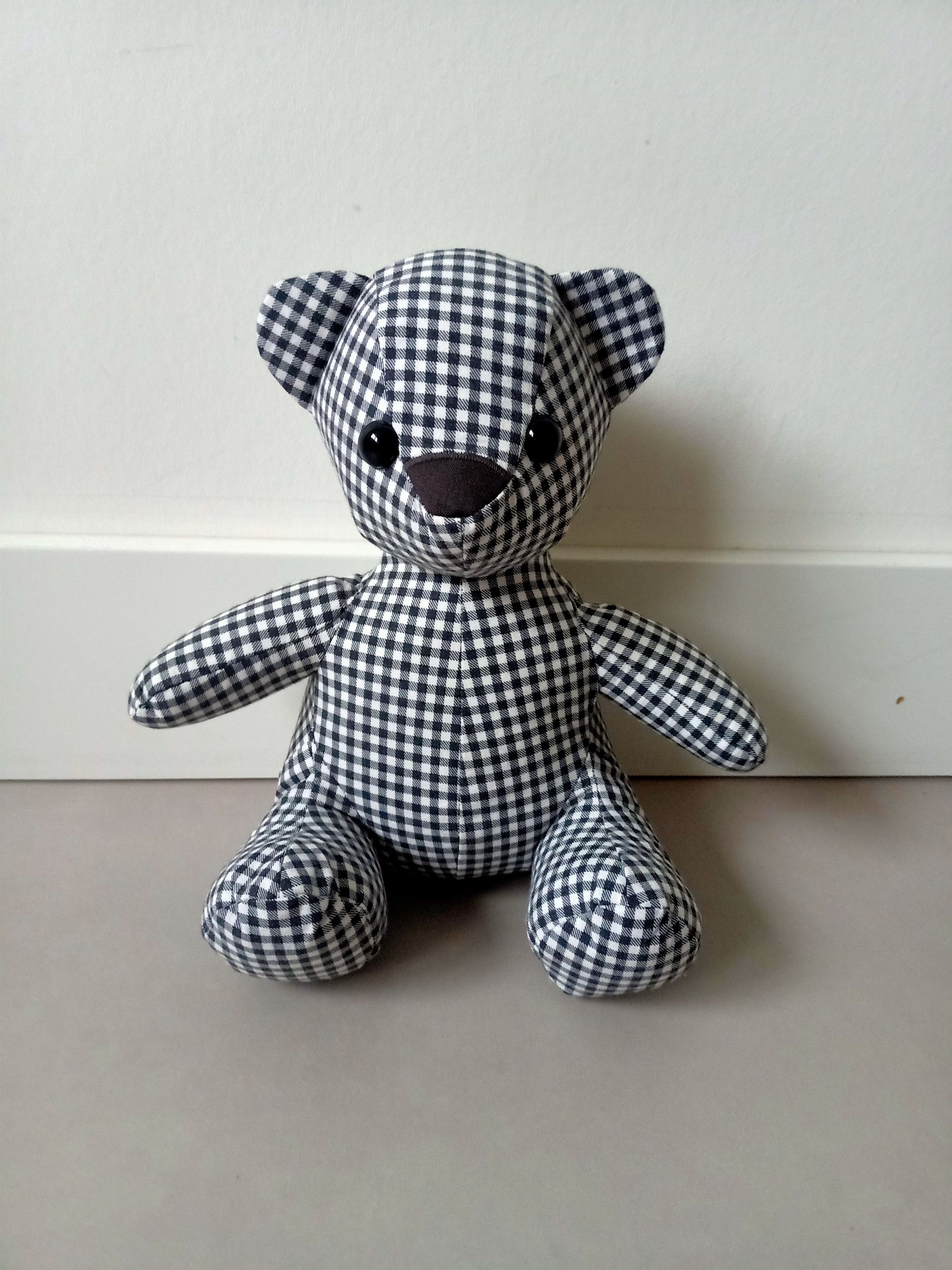 Een zwart-wit geblokte teddybeer zit op de grond en is gemaakt van een overhemd van opa