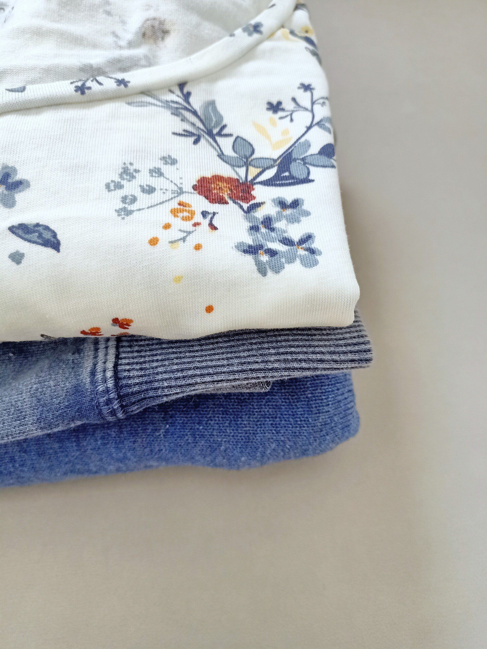 Een stapel kleding, waaronder een wit shirt met bloemen erop