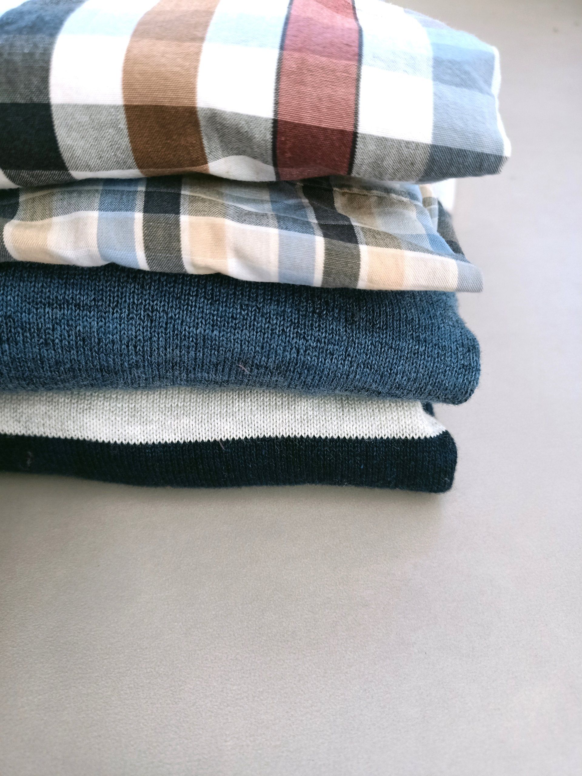 Een stapel kleding, waaronder een geruit overhemd en een trui