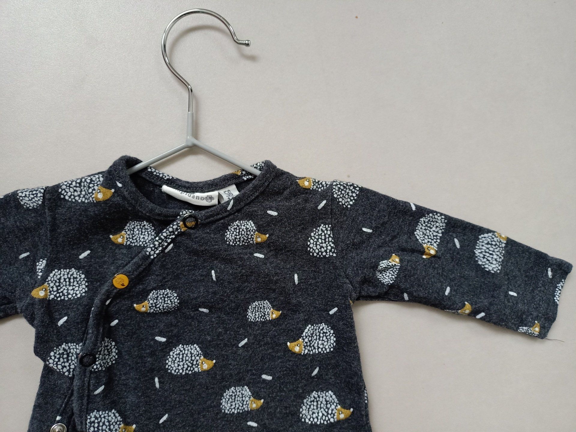 Een babyshirtje met egels erop hangt aan een hanger.