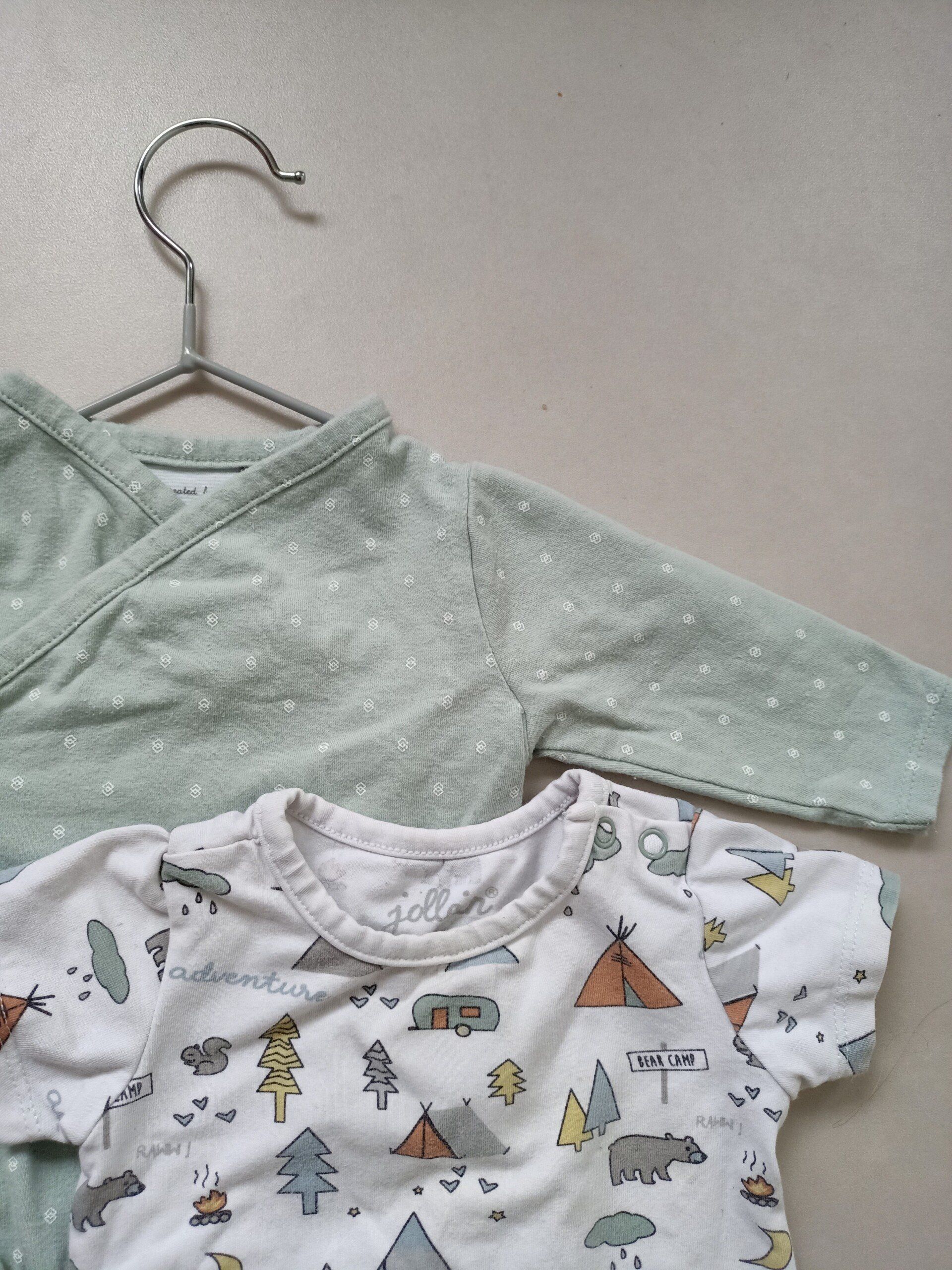 Twee babykleertjes hangen aan een hanger op een tafel.