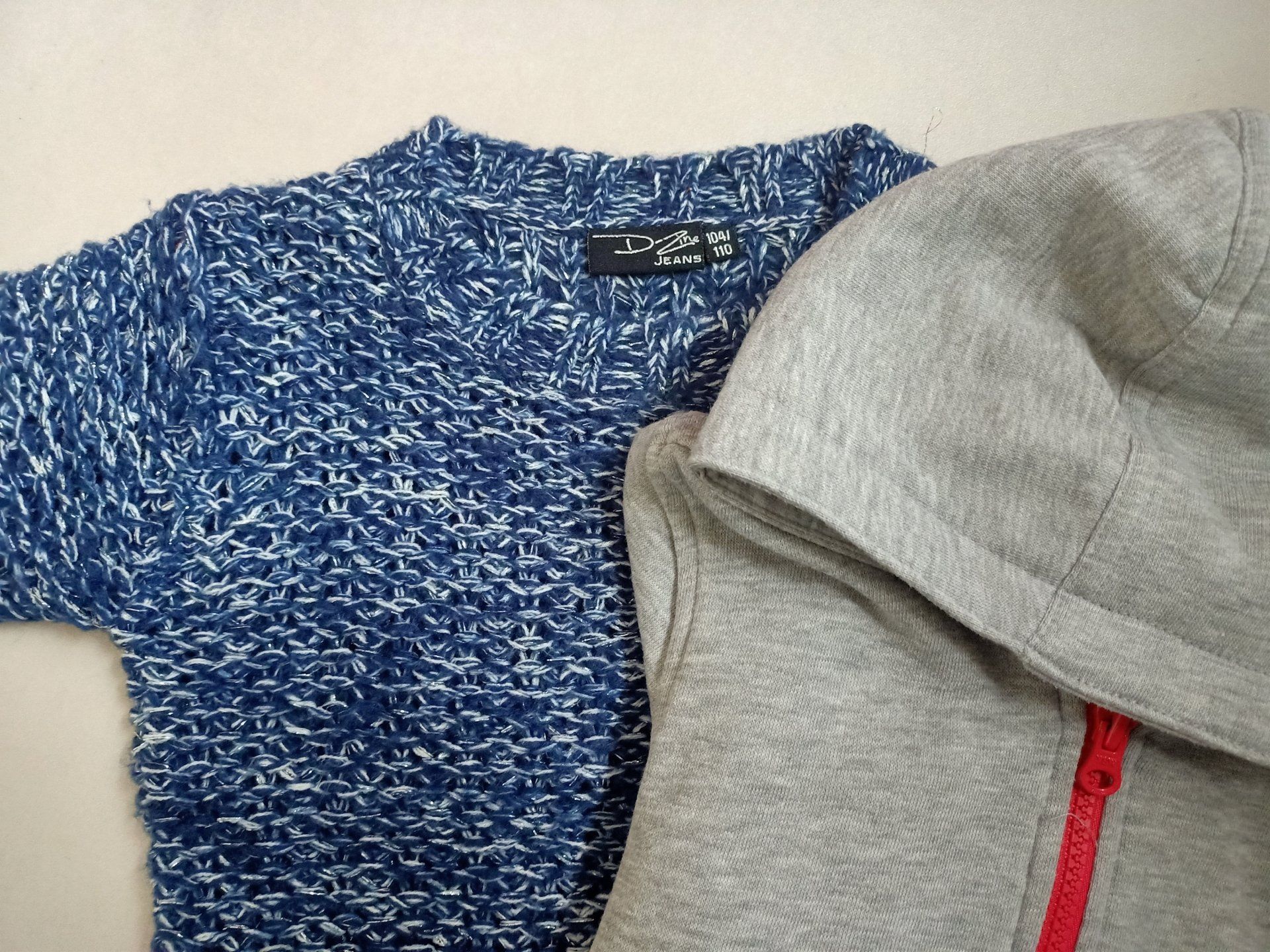 Een blauwe trui staat naast een grijze hoodie met een rode rits