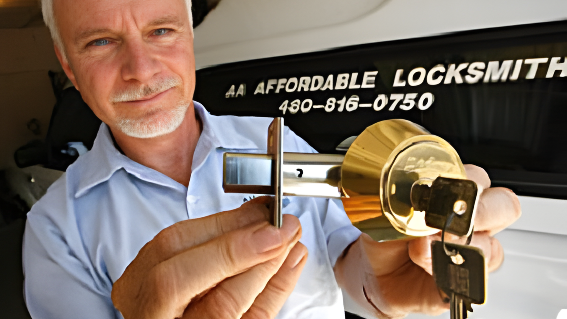 A locksmith holds a gold-colored deadbolt lock and keys in front of his service vehicle.