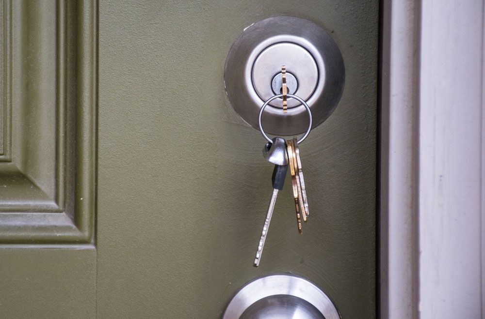 A set of keys hanging from the lock of a sage green door.