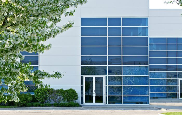 A modern, white office building exterior featuring large, grid-patterned glass windows and a double-door entrance.